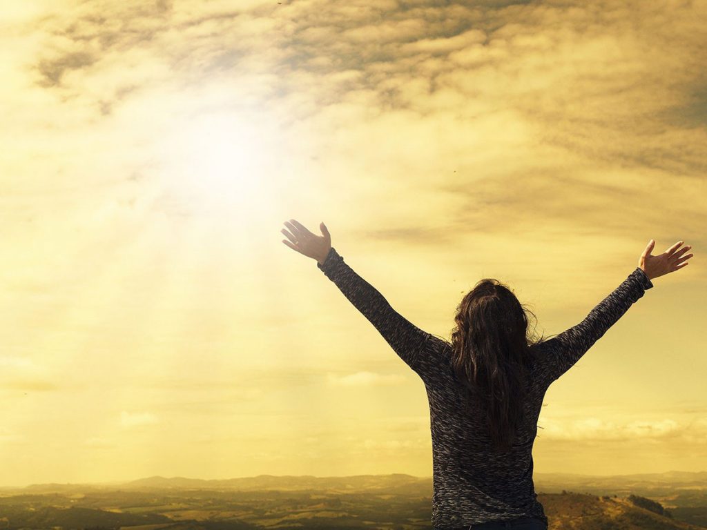Woman standing with open arms toward the sunlight | Share The Gift The Justice of God The Message